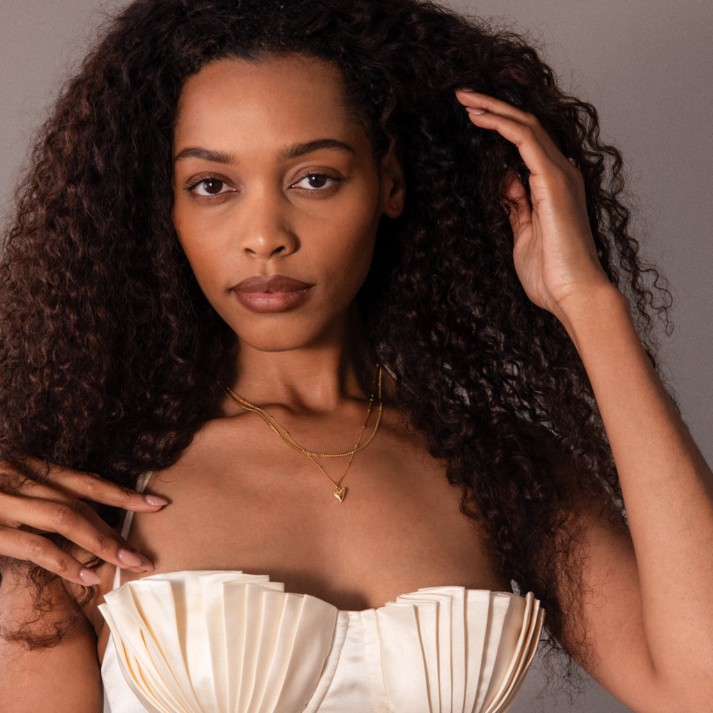 Woman with long curly hair wears a strapless cream top and the Shark Tooth Necklace, posing against a gray background.