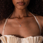 A woman wears a cream pleated top and the Shark Tooth Necklace, featuring a silver triangle pendant, for a chic beachside look.