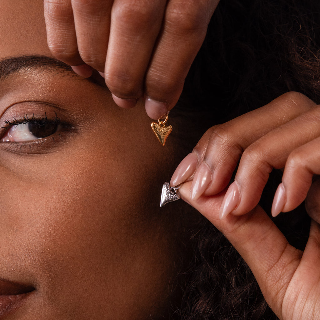 Close-up of a person holding a Dainty Shark Tooth Charm in Silver near their face, highlighting the beauty of coastal-inspired silver jewelry.