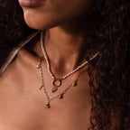 Close-up of a woman with curly hair wearing layered gold and pearl necklaces, featuring coastal jewelry and the Dainty Shark Tooth Charm in 18K Gold.