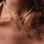 Close-up of layered gold necklaces with charms, a pearl strand, and the Dainty Shark Tooth Charm in 18K Gold, creating an elegant coastal jewelry look on the neck and collarbone.