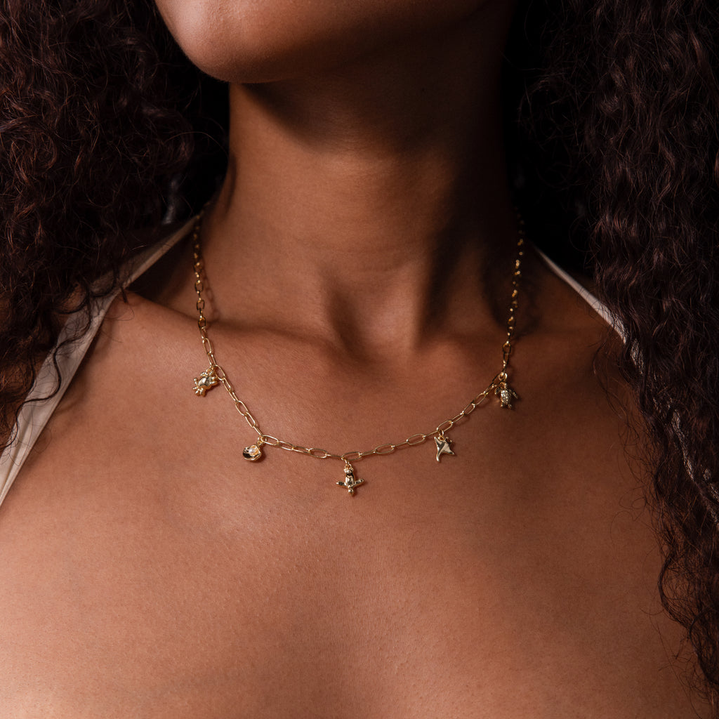Close-up of a woman wearing the Seaside Charm Necklace in 18K Gold, featuring small pendants, set against a neutral background.
