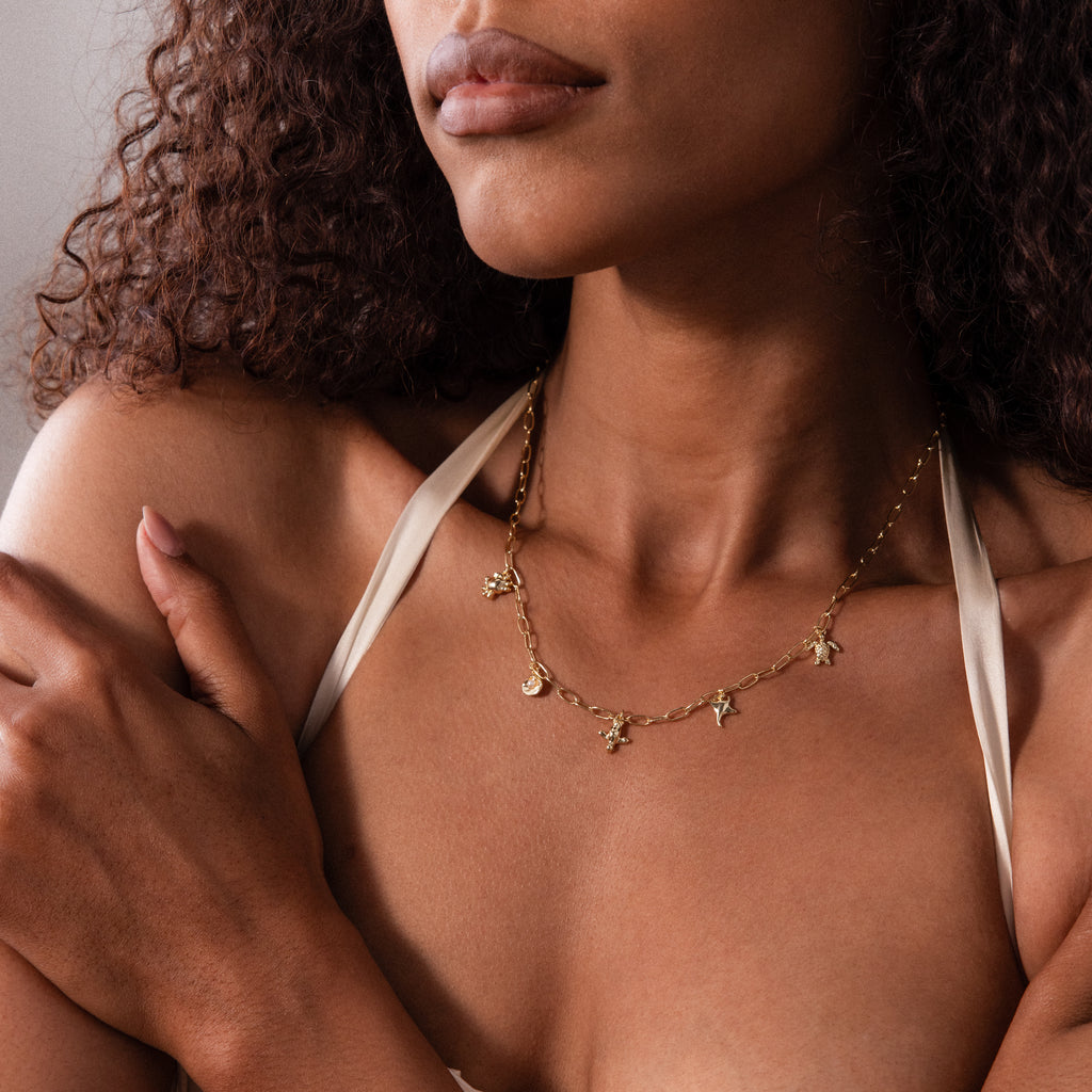 Woman wearing the Seaside Charm Necklace in 18K Gold and a cream satin top, arms crossed—an ideal beach jewelry choice for summer days.