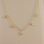 The Seaside Charm Necklace in 18K Gold features five delicate charms—a bird, leaf, flower, and round pendant—perfect beach jewelry for summer lovers of dainty style.