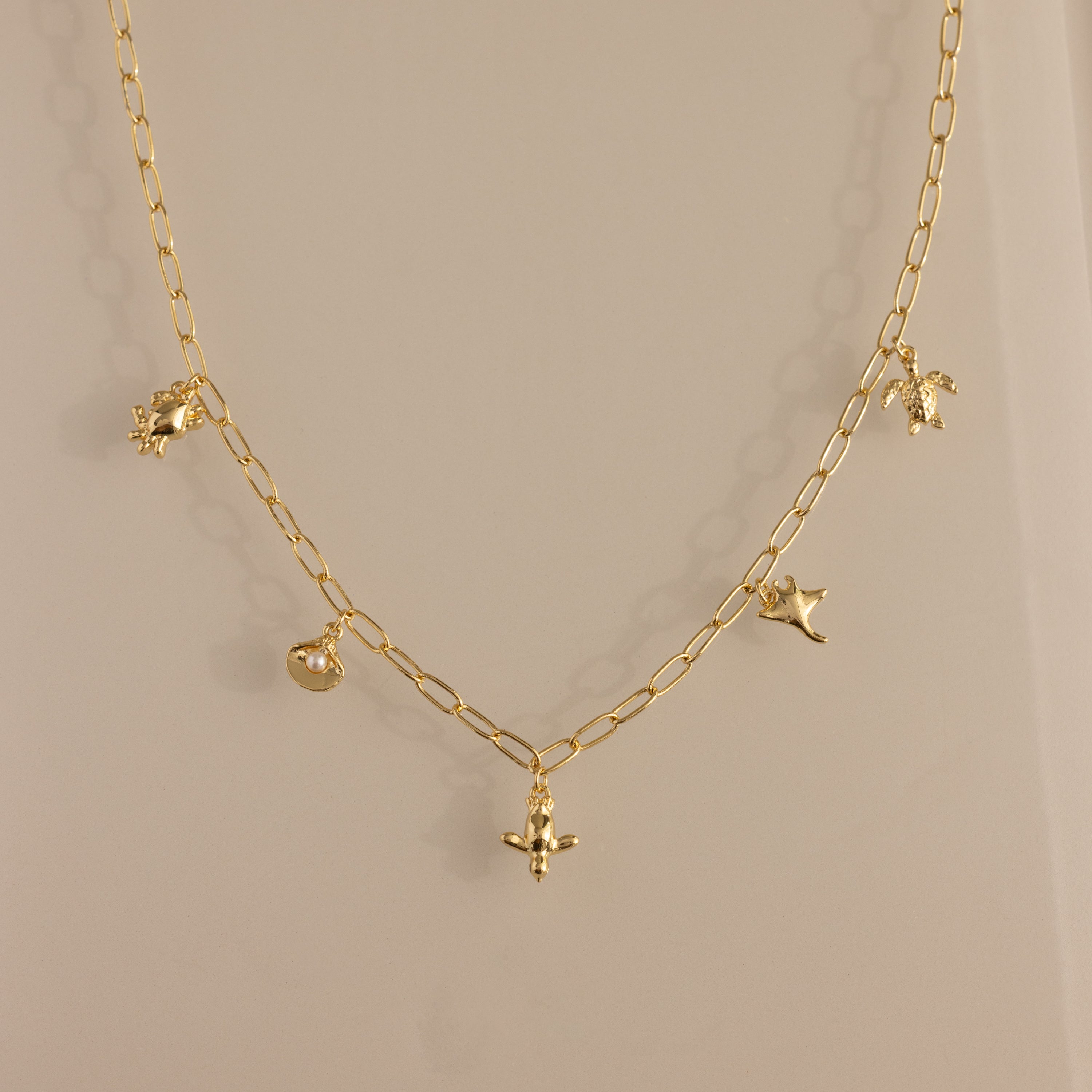 The Seaside Charm Necklace in 18K Gold features five delicate charms—a bird, leaf, flower, and round pendant—perfect beach jewelry for summer lovers of dainty style.