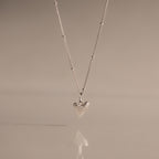 The Shark Tooth Necklace in Silver, displayed against a soft beige background, adds subtle coastal charm and beachside style to any look.