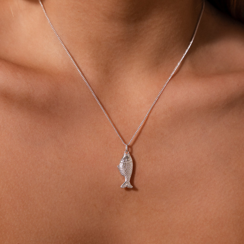 The Fish Pendant Necklace features a silver fish-shaped design, perfect for an ocean-inspired look or layering with your favorite jewelry.
