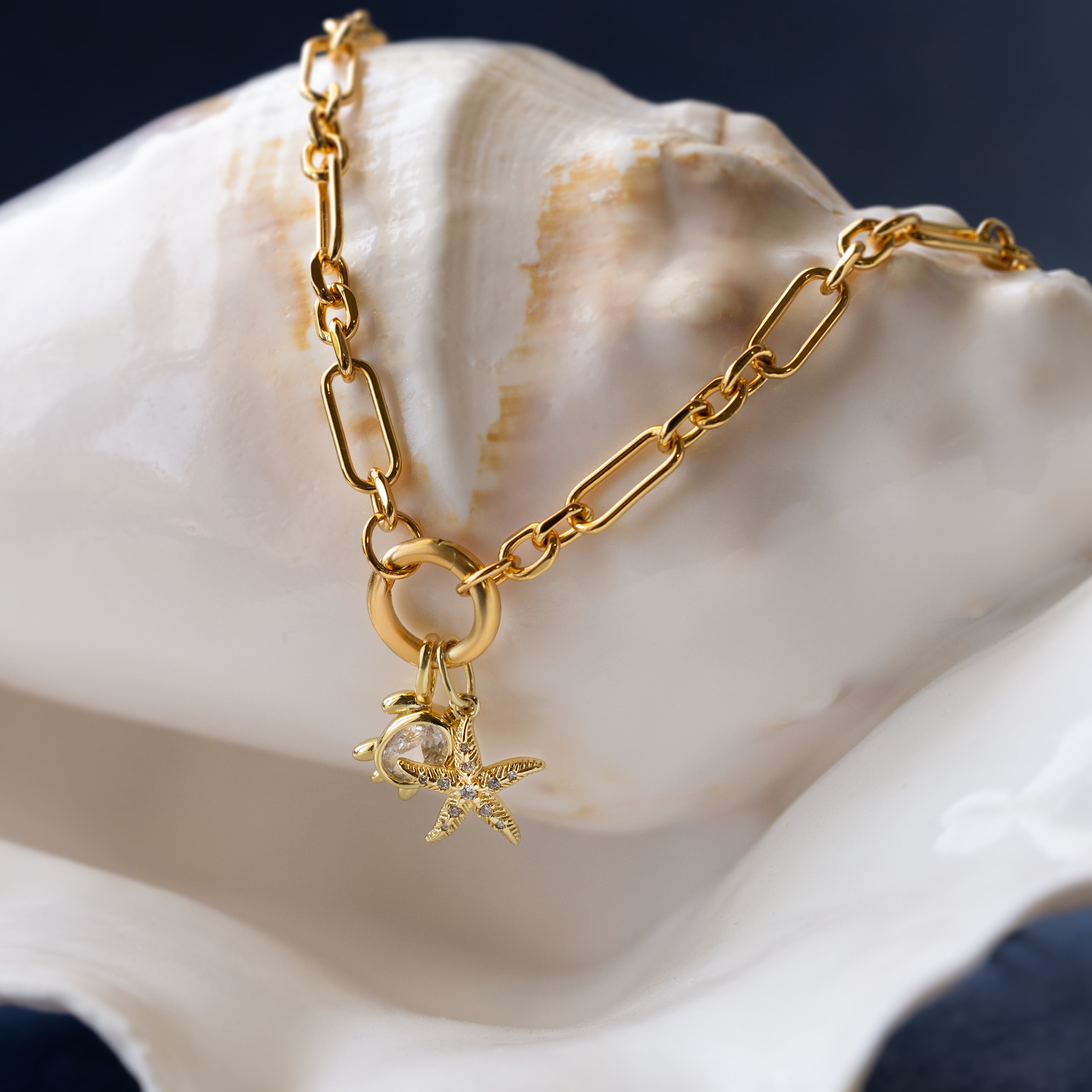 The Pave Starfish Charm in 18K Gold necklace features a sparkling starfish and seashells, perfect for adding coastal style to your collection. Displayed on a white seashell background.