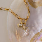 The Pave Starfish Charm in 18K Gold radiates coastal charm, resting on a pearly seashell alongside a gold chain and round gem.