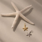 A white starfish highlights the Pave Starfish Charm in gold and silver on a soft, neutral background, showcasing its coastal elegance.