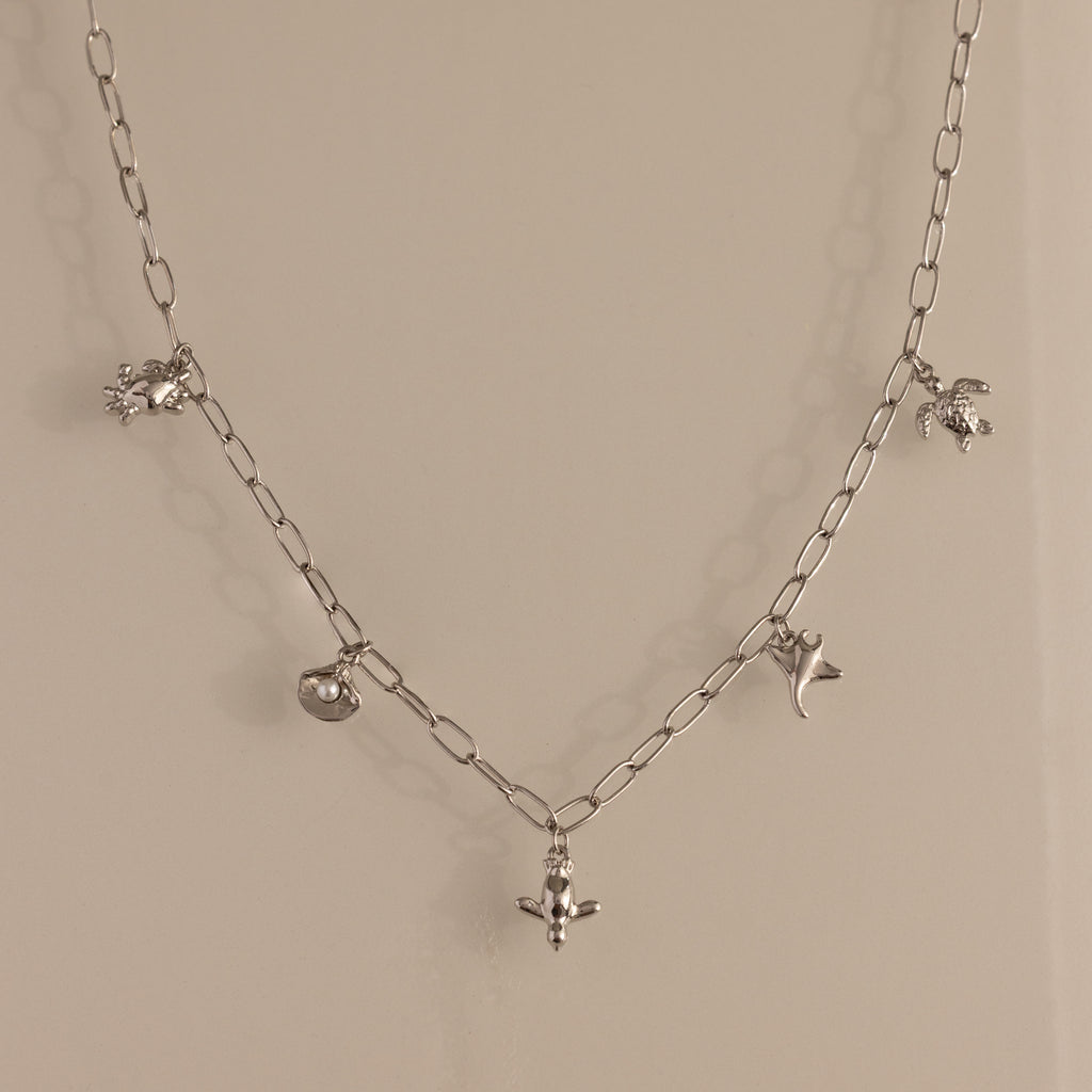 The Seaside Charm Necklace in Silver features five ocean-themed charms—crab, pufferfish, turtle, dolphin, and stingray—making it perfect beach jewelry for your summer necklace collection.