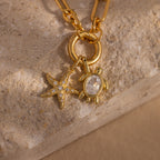 Diamond Turtle Charm: A gold necklace adorned with a diamond-studded turtle and starfish, both sparkling with gemstones, displayed on textured stone—a striking piece of ocean-inspired jewelry.