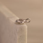 The Diamond Turtle Charm in Silver, featuring a sparkling gemstone, rests on a light marble surface—an ideal piece for admirers of ocean-inspired jewelry.