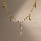 The Ocean Charm Necklace in 18K Gold features sea-themed charms—starfish, seahorse, shells, and pineapple—making it the perfect summer accessory on any neutral background.