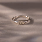 The Hand & Footprint Signet Ring in Sterling Silver features tiny engraved hand and footprints on a polished surface—ideal as a cherished baby keepsake, beautifully displayed on a light background.