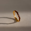The Staggered Marquise Garnet Ring shines with red gemstones, casting a shadow on a softly lit neutral surface.