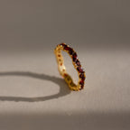 The Staggered Marquise Garnet Ring shines with red gemstones, casting a shadow on a softly lit neutral surface.