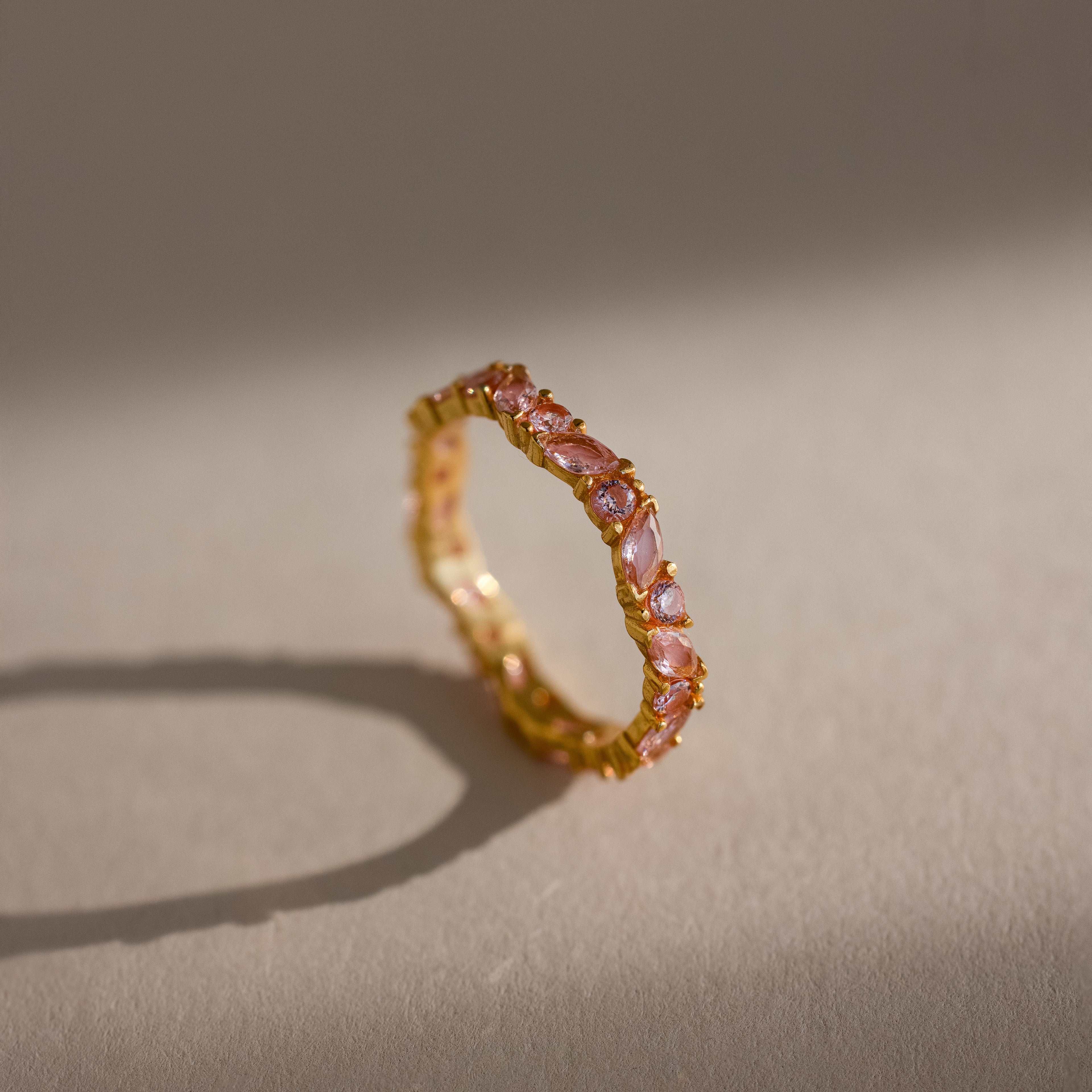 The Staggered Marquise Pink Tourmaline Ring features vibrant gemstones that cast a delicate shadow on a neutral surface.