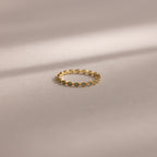 The Dainty Marquise Blue Zircon Ring, a delicate Art Deco-inspired gold piece with a shimmering blue zircon, rests on a soft beige surface with gentle shadow lines.