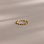 The Dainty Marquise Peridot Ring, featuring a delicate gold Art Deco-inspired twisted design, rests on a soft, neutral surface.