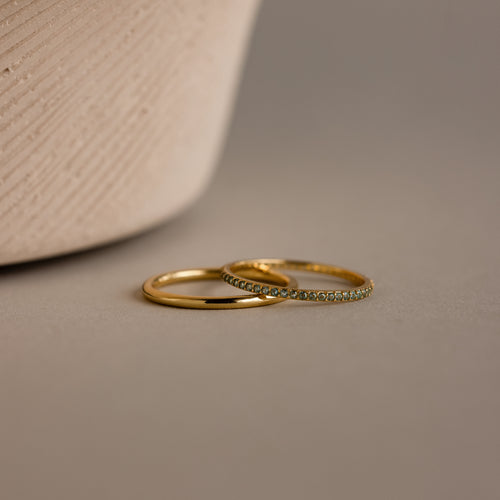 The Birthstone Tennis Ring Set in Aquamarine (March) features two elegant rings—a sleek gold band and a gemstone eternity ring—gracefully displayed on a neutral surface.