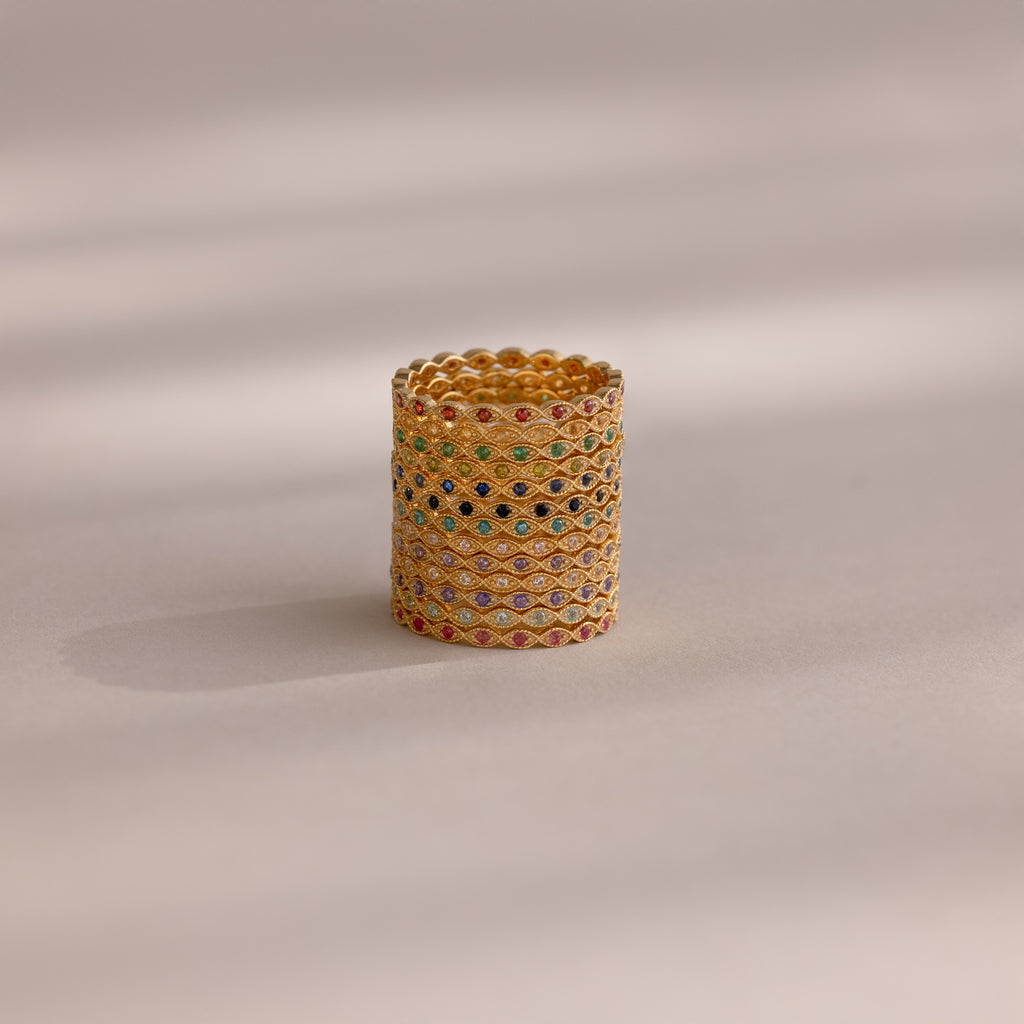 The Dainty Marquise Topaz Ring, featuring diamond-shaped patterns and multi-colored gemstones, is displayed upright alongside other gold rings on a neutral background with soft lighting.