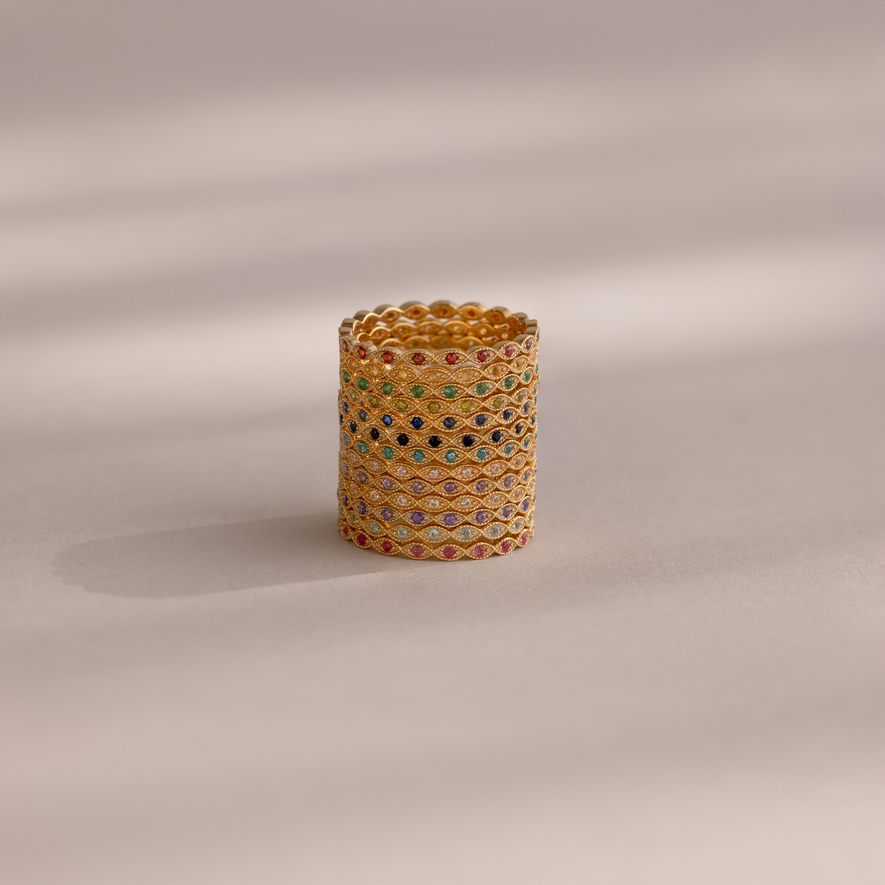 The Dainty Marquise Topaz Ring, featuring diamond-shaped patterns and multi-colored gemstones, is displayed upright alongside other gold rings on a neutral background with soft lighting.