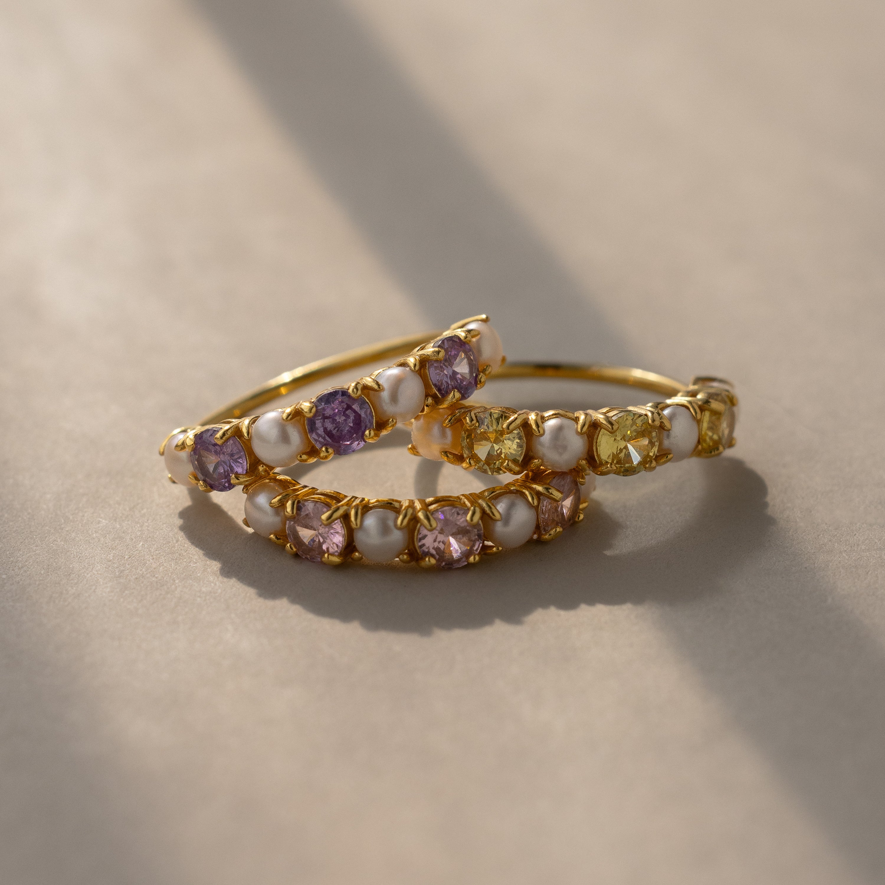Two gold bands set with alternating pastel gemstones in shades of purple, yellow, and white, perfect as a delicate birthstone accessory and displayed on a neutral surface under soft lighting.