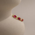 The Pink Ruby & Pearl Lace Ring, featuring alternating pink gemstones and pearls, rests on a smooth, curved beige surface.