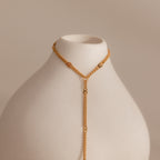 Curb hand chain bracelet in 18K gold displayed on a white ceramic prop.