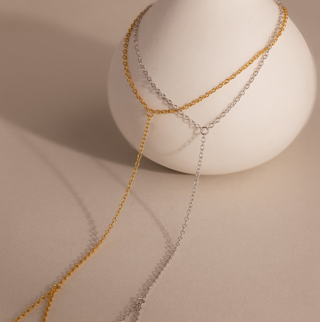 The Dainty Hand Chain Bracelet in 18K Gold is elegantly displayed over a smooth white vase on a beige background, perfect for anyone who loves delicate, minimalist jewelry.