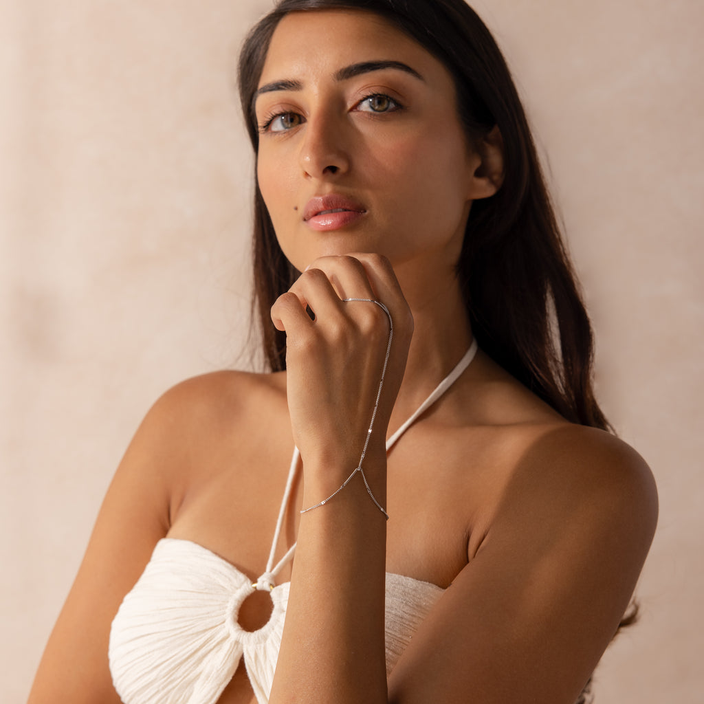 Model wearing a sterling silver hand chain bracelet that connects to a delicate finger loop.