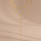 Close-up of a gold dainty Sparkling Layered Lariat Necklace, featuring 3 layers of mirror chain necklaces in varying lengths.