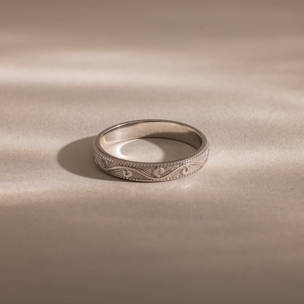 The Filigree Ring in Sterling Silver, featuring vintage-inspired engraved patterns, rests on a smooth, light surface under soft lighting.