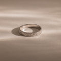 The Filigree Ring in Sterling Silver, featuring vintage-inspired engraved patterns, rests on a smooth, light surface under soft lighting.