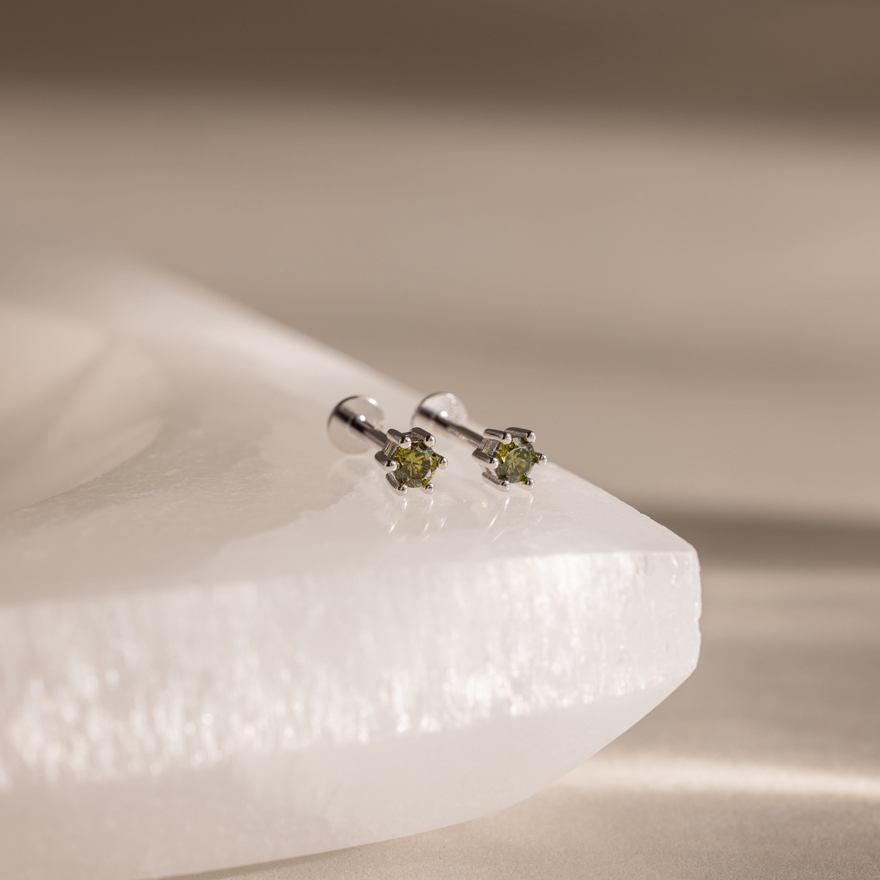 Peridot Flatback Studs featuring green gemstones set in silver, displayed on a white faceted surface.