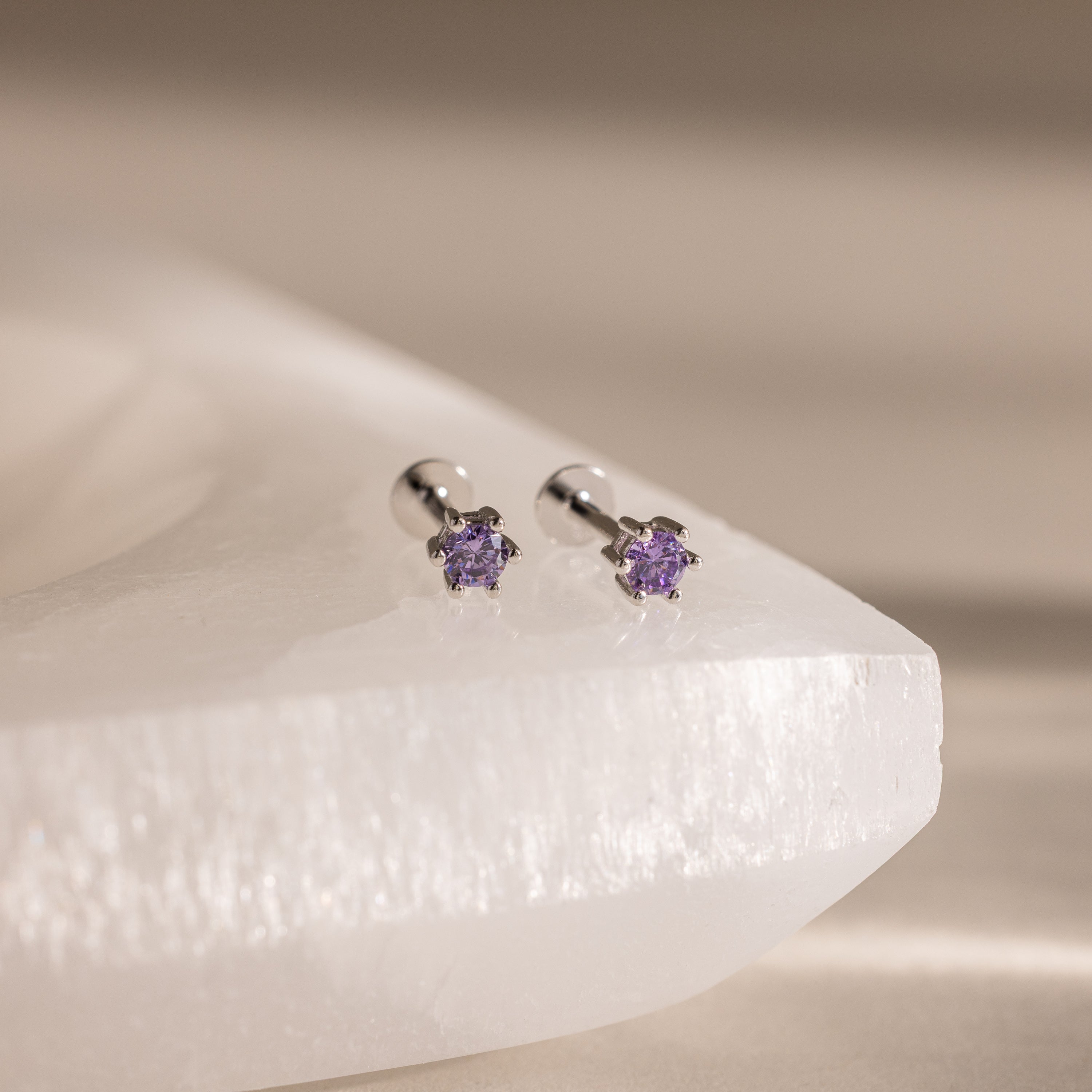 Amethyst Flatback Studs—silver earrings featuring small purple gemstones, shown on a white textured surface.