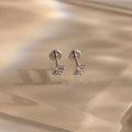 Pair of silver geometric flat back diamond stud earrings on a reflective gold surface