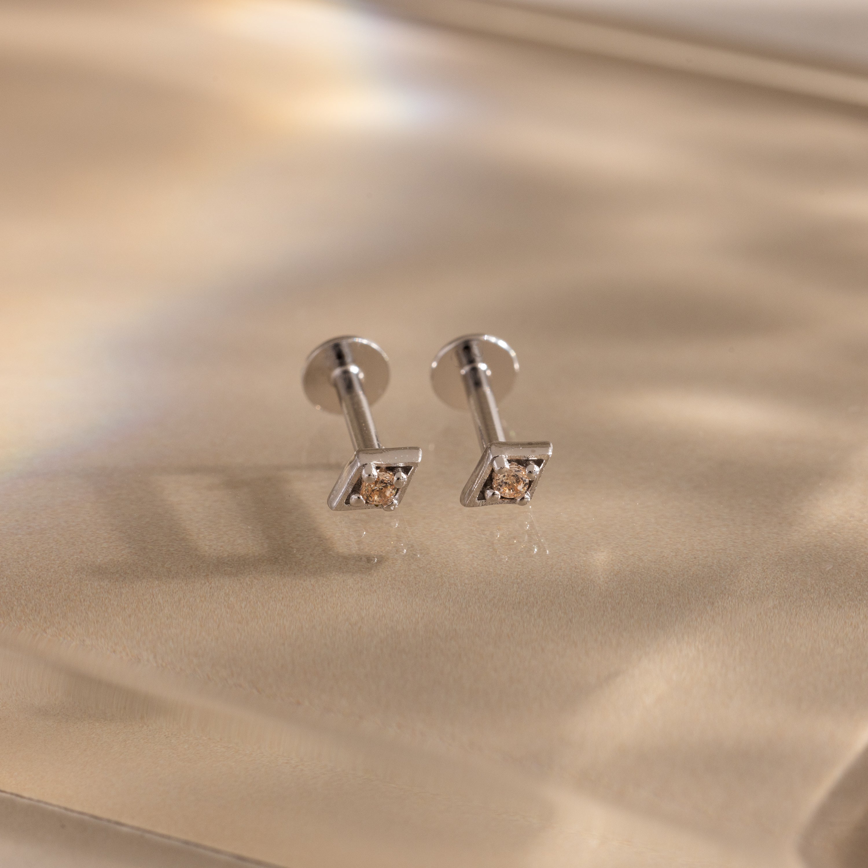 Pair of silver geometric flat back topaz stud earrings on a beige background