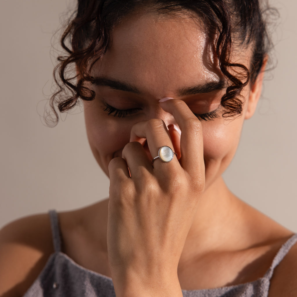A woman smiles with her eyes closed, touching her nose, while wearing a vintage-inspired Mother of Pearl Signet Ring in Sterling Silver featuring a white stone.