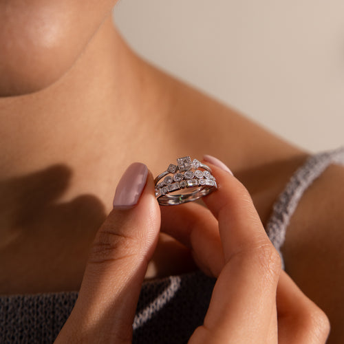 Close-up of model holding a stacked silver Art Deco ring set with various diamond cuts, near her shoulder in soft lighting.