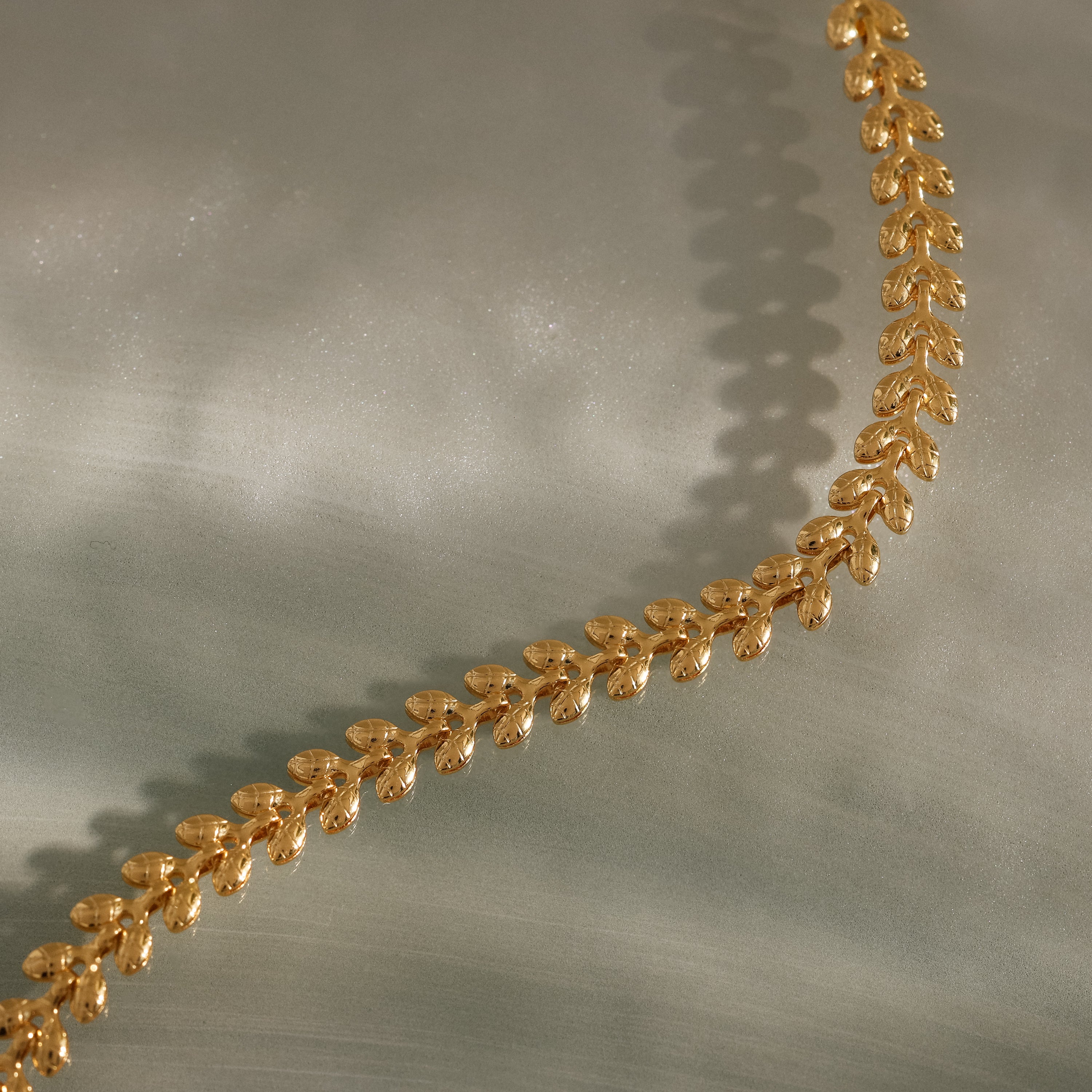 The Fishtail Chain Bracelet in 18K Gold features intricately interwoven links and exquisite craftsmanship, elegantly displayed on a smooth, light-colored surface.