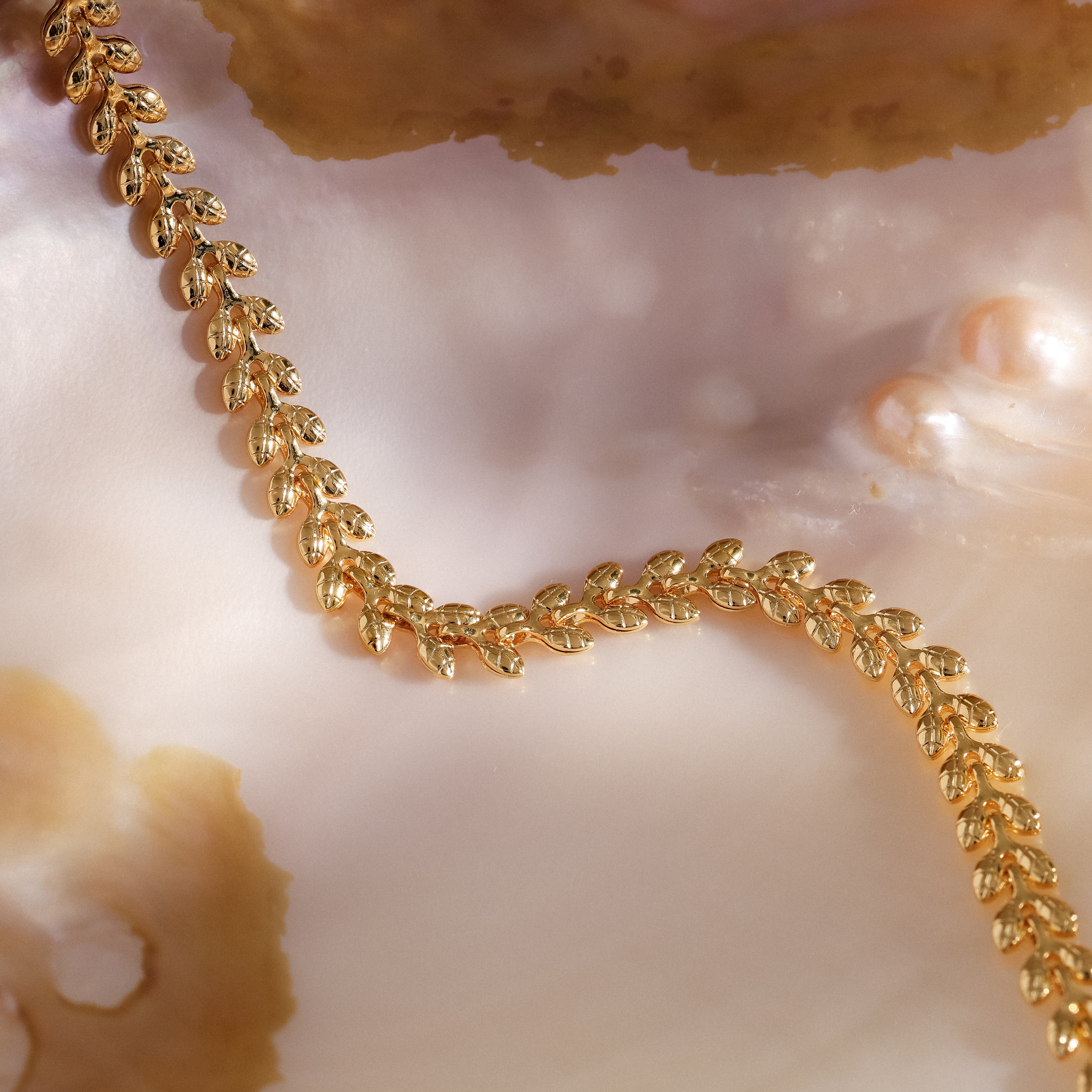 The Fishtail Chain Bracelet in 18K Gold features interwoven links, elegantly displayed on a pearly shell background to highlight its intricate craftsmanship.