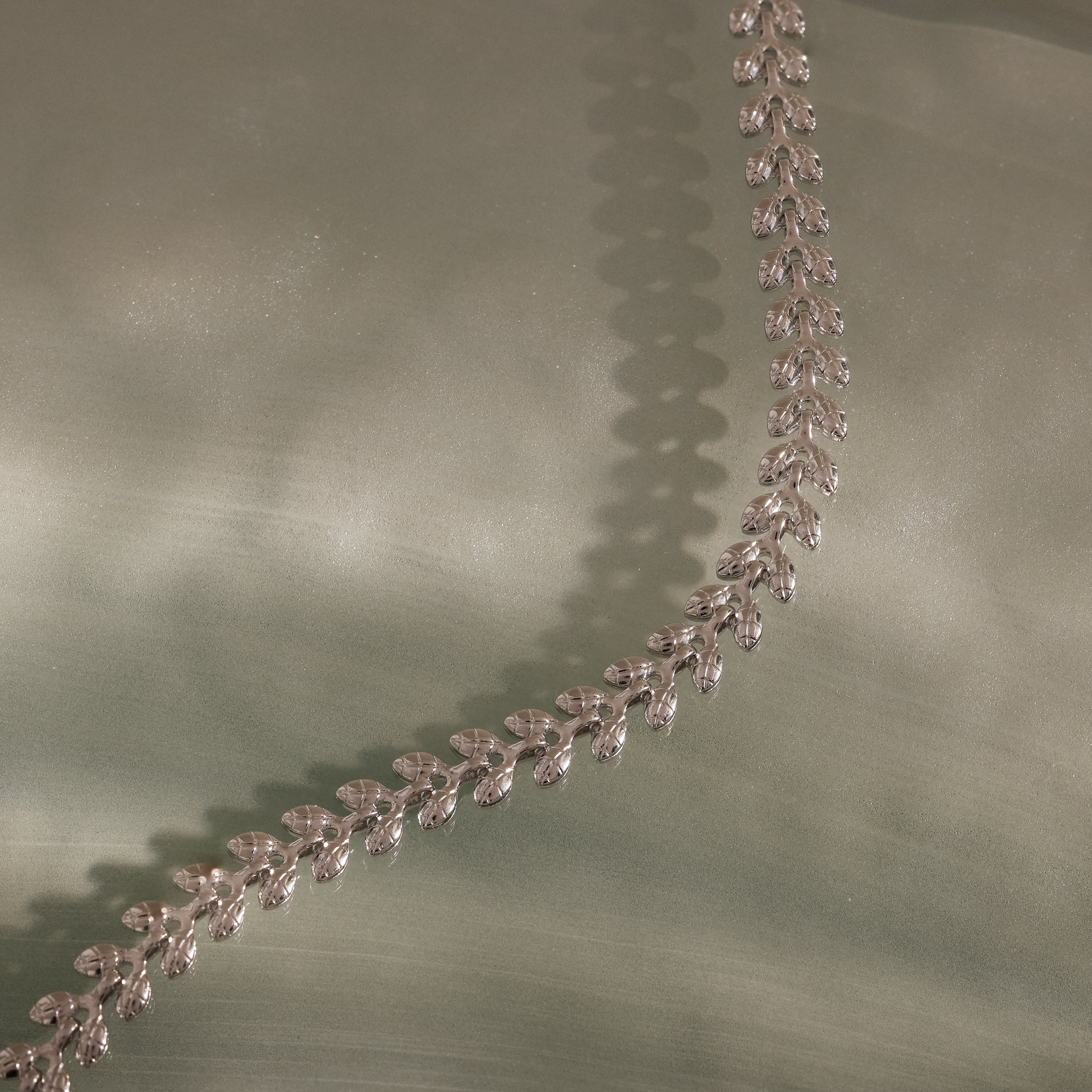 The Fishtail Chain Bracelet is displayed on a soft, light green surface.