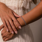 A woman with manicured nails, wearing a cream lace dress, crosses her hands to showcase the detailed craftsmanship and cascading texture of the Fishtail Chain Bracelet.