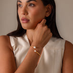 Woman in a sleeveless cream top wears the Serenity Pearl Cuff Bracelet in 18K Gold, featuring a modern open band with two pearls, while looking to the side.