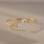 The Serenity Pearl Cuff Bracelet in 18K Gold features two white pearls on each end and a sleek open band, creating a modern and elegant jewelry piece.
