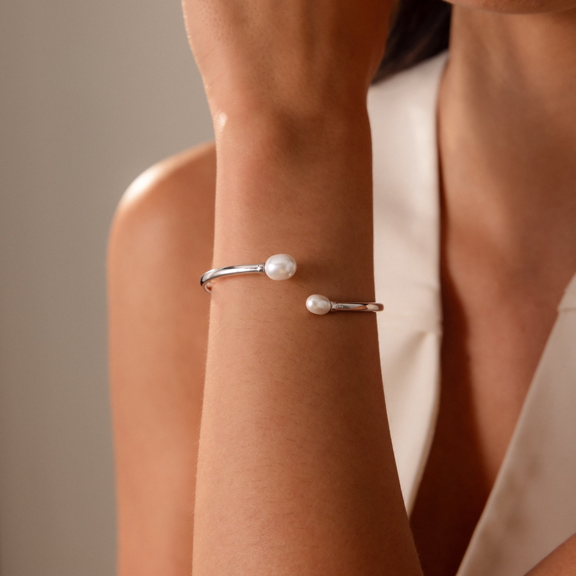 A woman wearing the Serenity Pearl Cuff Bracelet in Silver on her wrist, paired with a sleeveless white top.