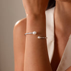A woman in a sleeveless top wears the Serenity Pearl Cuff Bracelet, featuring two white pearls—a modern and elegant jewelry choice.