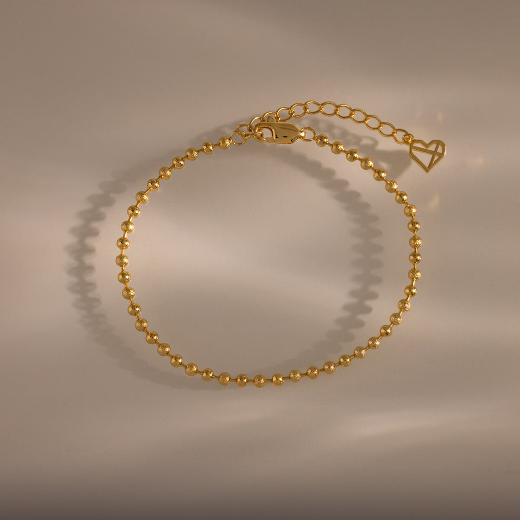 Dune Beaded Bracelet in 18K Gold features polished beads, an adjustable chain, and a heart charm, displayed on a neutral background.